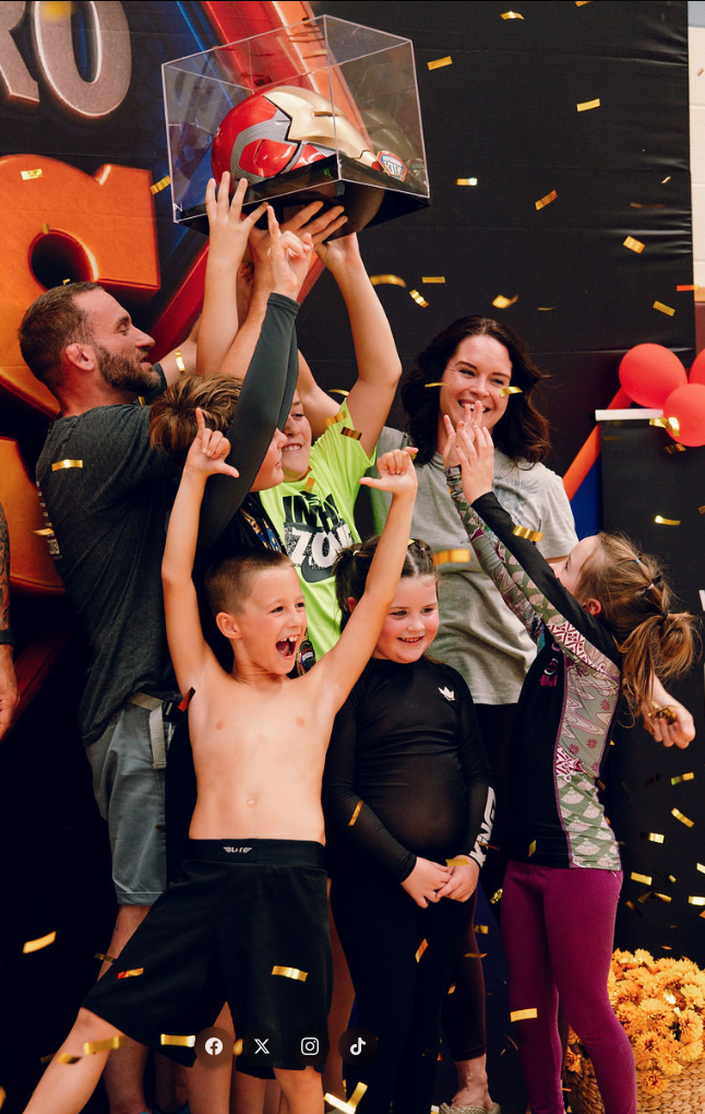 Young athletes and families celebrating with the champion trophy under gold confetti at Superhero Kids Nampa