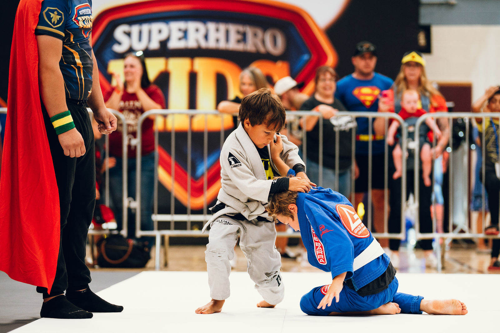 A coach supporting a young athlete from the corner of the mat at Superhero Kids Nampa